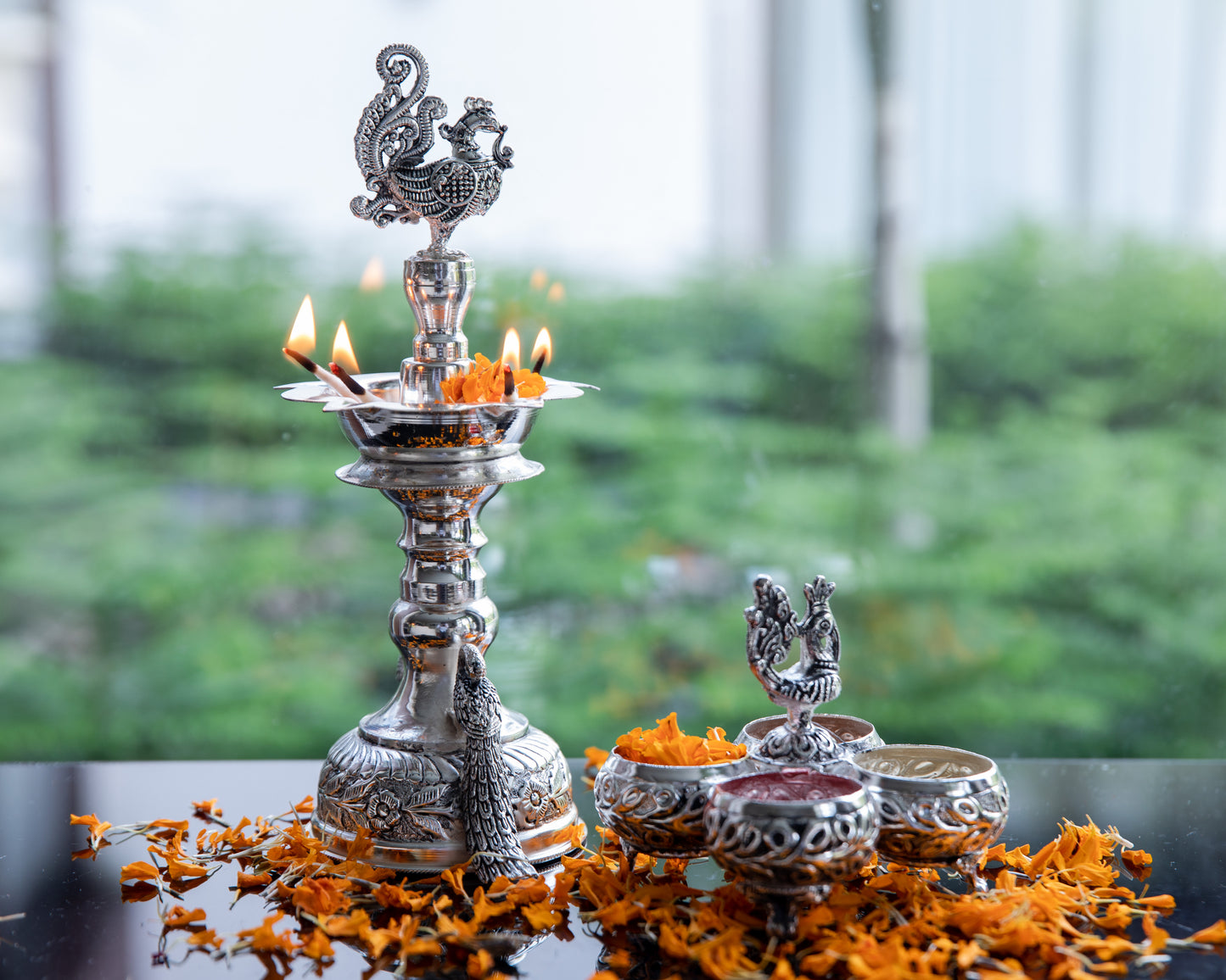 Our Silver Peacock Tall Diya is coated with premium silver plating, this diya stand radiates a lustrous and timeless glow when the diya is lit. It holds five wicks of diya.