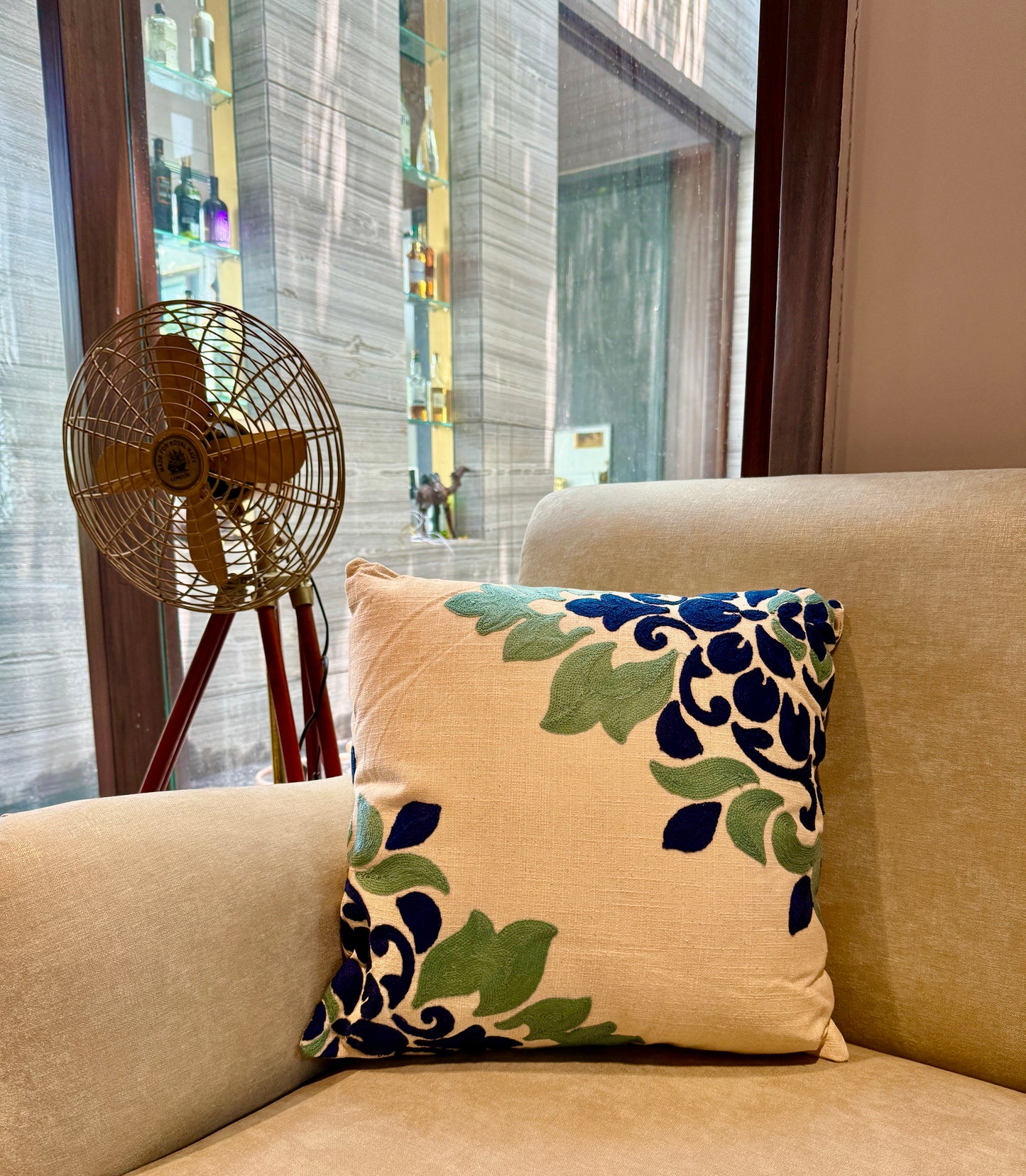 Hand-embroidered in deep navy and sage tones on a soft beige canvas, this cushion brings subtle drama to any sofa or accent chair.