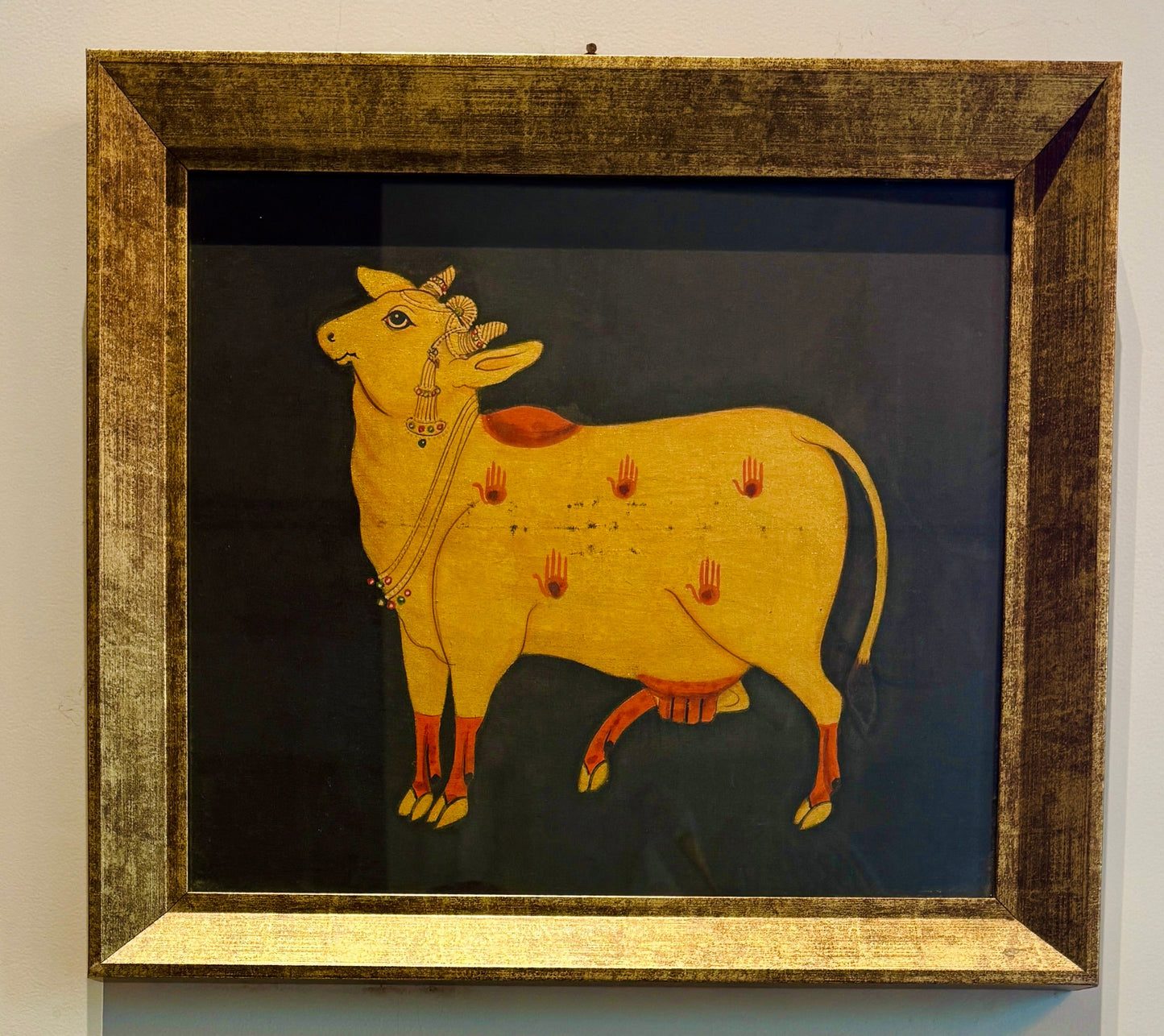 Hand-painted with real gold | Framed | Origin: Udaipur, Rajasthan This Udaipuri Pichvai captures Kamadhenu — the divine cow believed to grant all desires. Painted using natural pigments and real gold detailing, the artwork reflects the sacred richness of traditional temple murals.