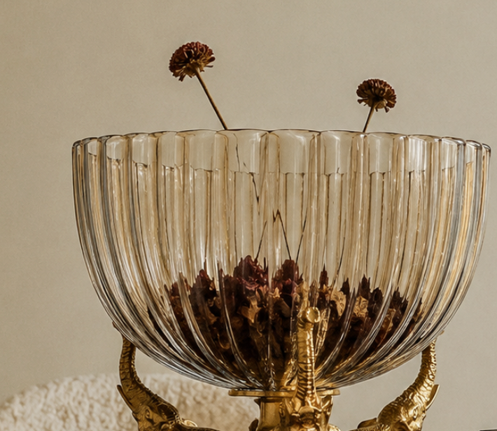 A statement decorative bowl where three brass elephants stand trunk-to-tusk, their raised trunks cradling a fluted, amber-tinted glass bowl above.