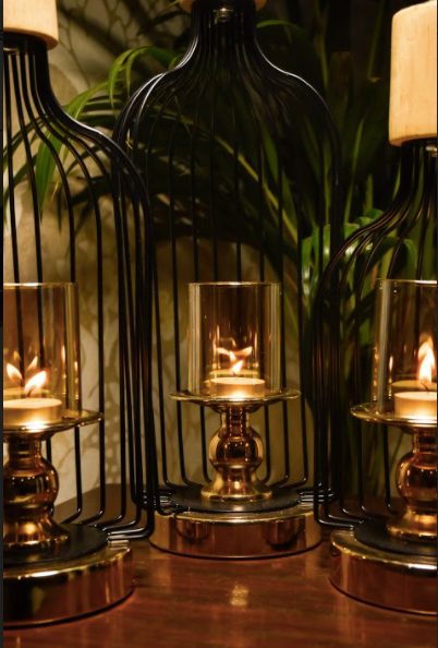 A Set of 3, are made of metal, in a glossy black finish supported by a metal base underneath, that comes in a chrome gold finish. The Murk Metal Lanterns are partially open on one end to keep your choice of candles within the glass candle holder that is supported by another metal stand within, on which it is mounted upon.