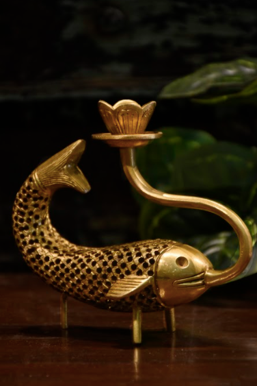 A Brass Candle Stand, Moulded in the form of a fish, , with the provision to hold a pencil candle, supported by three brass legs for stability.