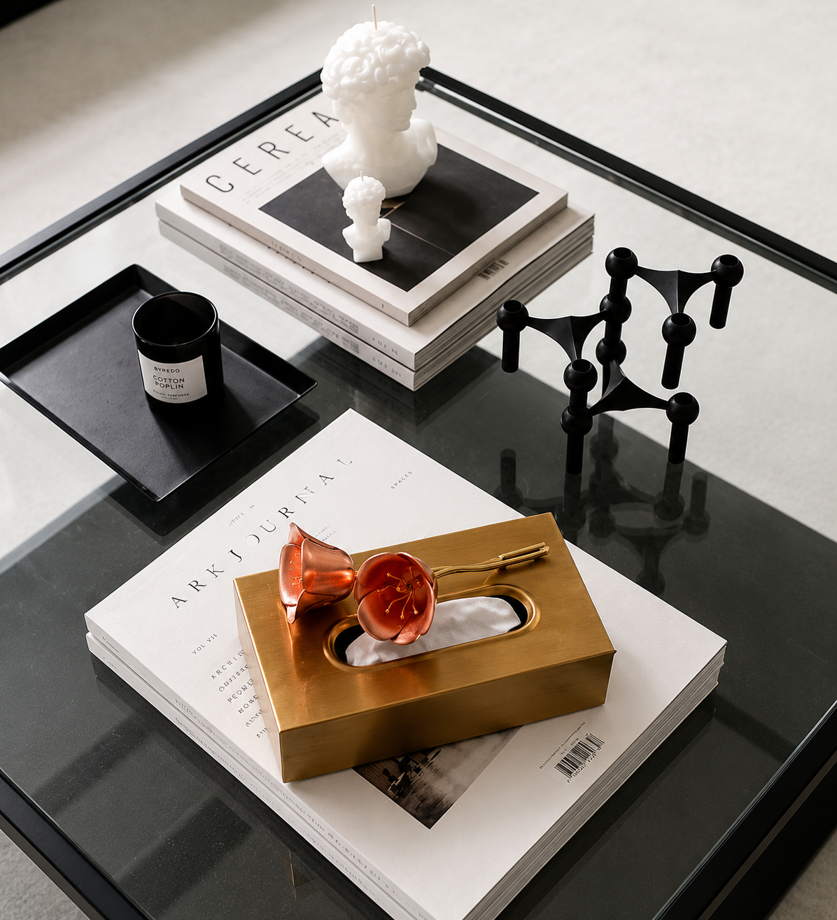 A striking rectangular tissue box in a brushed brass-plated finish, topped with an oversized resin flower in a warm coral-red hue that curls delicately across the lid. 