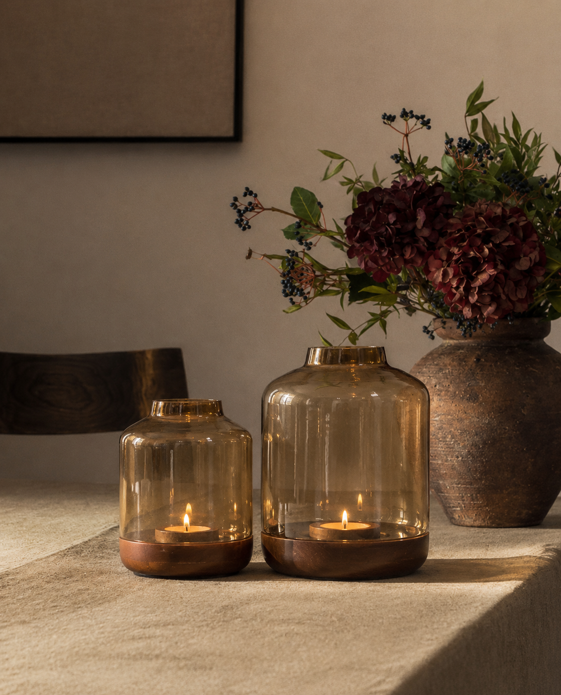 Jar-shaped lanterns in warm, smoked amber glass, each set on a solid wood base with a raised rim to hold a tealight securely. 
