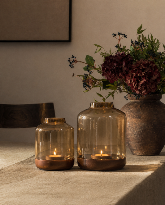 Jar-shaped lanterns in warm, smoked amber glass, each set on a solid wood base with a raised rim to hold a tealight securely. 