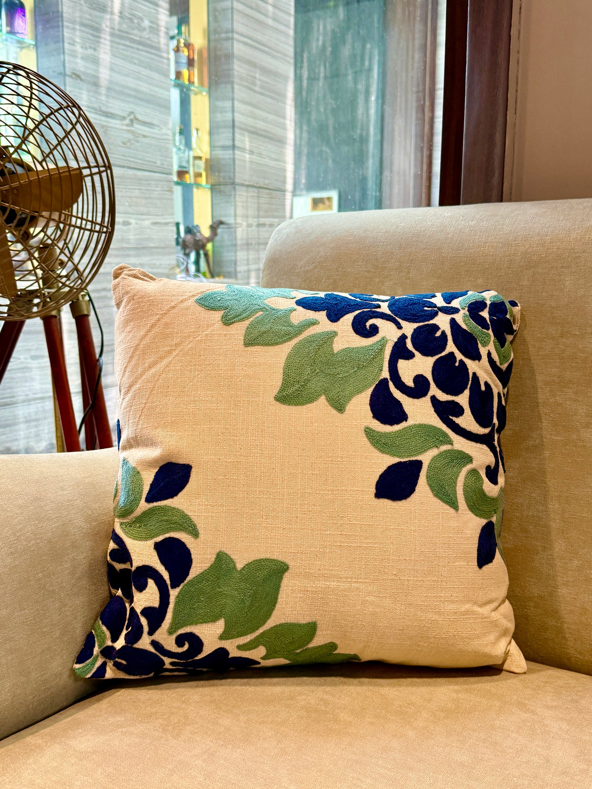  Hand-embroidered in deep navy and sage tones on a soft beige canvas, this cushion brings subtle drama to any sofa or accent chair. 