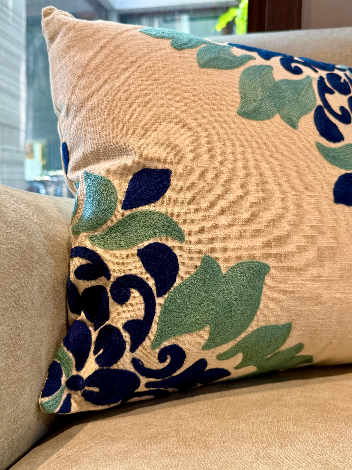  Hand-embroidered in deep navy and sage tones on a soft beige canvas, this cushion brings subtle drama to any sofa or accent chair. 