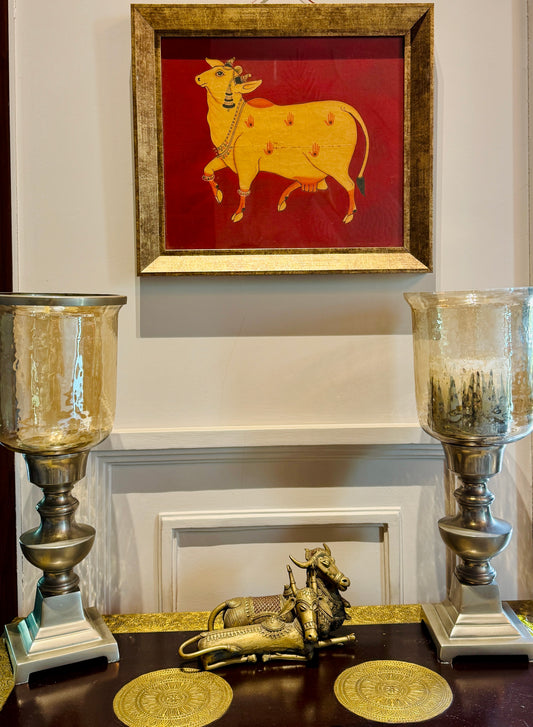 Hand-painted with real gold | Framed | Origin: Udaipur, Rajasthan This Udaipuri Pichvai captures Kamadhenu — the divine cow believed to grant all desires. Painted using natural pigments and real gold detailing, the artwork reflects the sacred richness of traditional temple murals. 