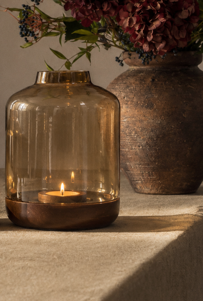 Jar-shaped lanterns in warm, smoked amber glass, each set on a solid wood base with a raised rim to hold a tealight securely. 