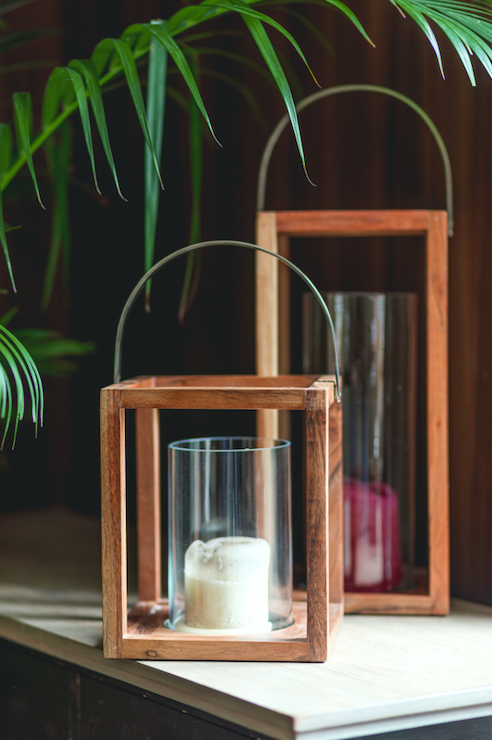 Structural wooden lanterns made of mango wood with a metal handle on top and a cylindrical glass candle holder within