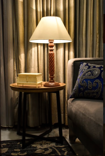 A wooden lamp made with mango wood, carved with elegant detailing along with a beige lamp shade.