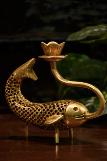 A Brass Candle Stand, Moulded in the form of a fish, , with the provision to hold a pencil candle, supported by three brass legs for stability. 
